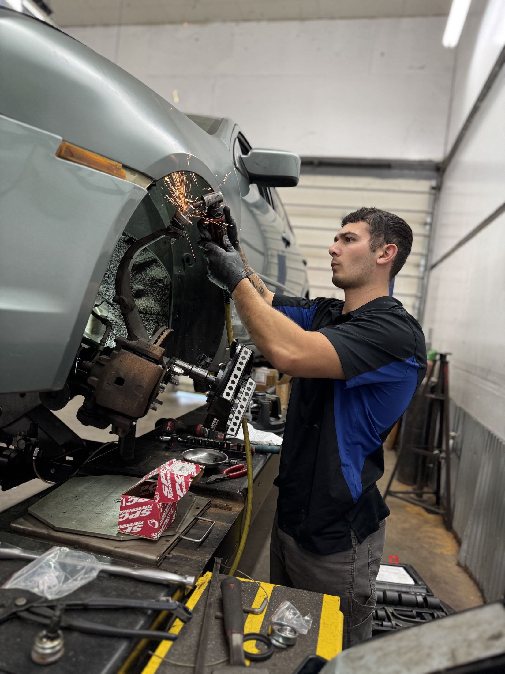 Dartt Automotive technician grinding a front strut assembly, sparks flying